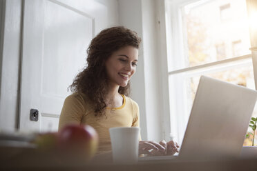 Lächelnde junge Frau zu Hause am Laptop - RBF002260