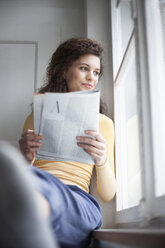 Lächelnde junge Frau beim Lesen einer Zeitschrift am Fenster - RBF002276