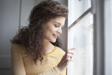 Lächelnde junge Frau malt Herz auf Fensterscheibe - RBF002278