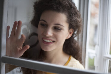 Lächelnde junge Frau malt Herz auf Fensterscheibe - RBF002280