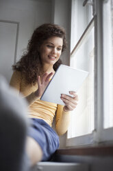 Lächelnde junge Frau mit digitalem Tablet am Fenster - RBF002281