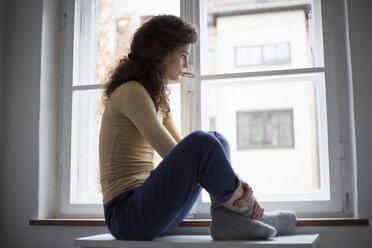 Traurige junge Frau schaut aus dem Fenster - RBF002282