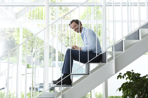 Businessman using laptop on office staircase stock photo