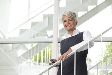 Smiling mature businesswoman on office staircase - MFRF000051