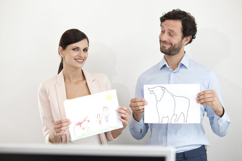Businesswoman holding child's drawing and businessman holding paper with bull figure - MFRF000030