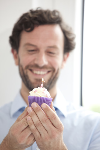 Lächelnder Geschäftsmann mit Geburtstagstörtchen, lizenzfreies Stockfoto