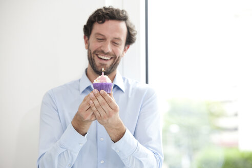 Smiling businessman holding birthday cupcake - MFRF000036