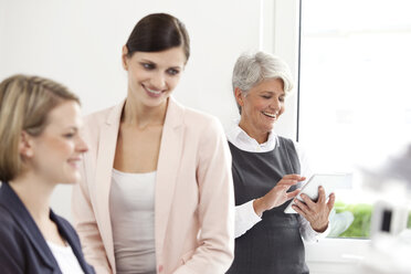 Drei lächelnde Geschäftsfrauen mit digitalem Tablet im Büro - MFRF000040