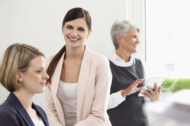 Drei lächelnde Geschäftsfrauen mit digitalem Tablet im Büro - MFRF000041