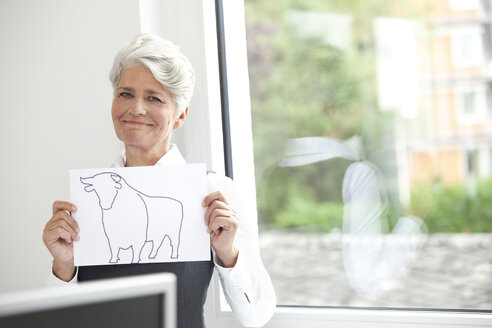 Smiling mature businesswoman holding paper with bull figure - MFRF000010