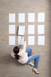 Businesswoman sitting on floor organizing blank sheets of paper - MFRF000043