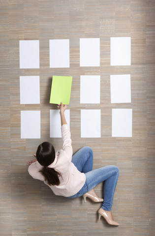 Businesswoman sitting on floor organizing blank sheets of paper stock photo