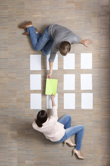 Businessman and businesswoman sitting on floor organizing blank sheets of paper - MFRF000045