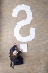 Businesswoman sitting on floor with blank sheets of paper in shape of question mark - MFRF000046