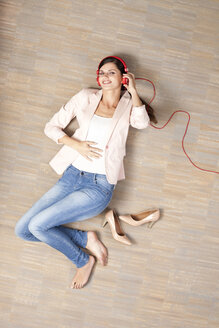Young woman lying on floor listening to music - MFRF000047