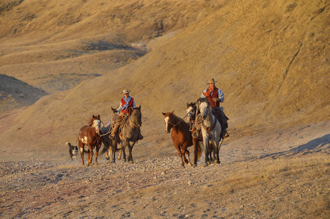 USA, Wyoming, Cowboy und Cowgirl führen Pferde in den Badlands, lizenzfreies Stockfoto