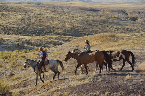 USA, Wyoming, Cowboy und Cowgirl führen Pferde in den Badlands - RUEF001469