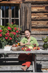 Smiling young woman sitting in front of Alpine cabin with cold snack - HHF005087