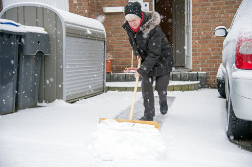 Germany, Grevenbroich, woman shoveling snow in front of house - FRF000188