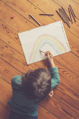 Girl lying on timber floor drawing rainbow stock photo