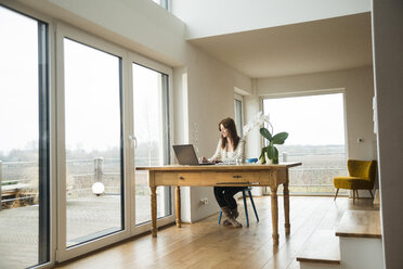 Junge Frau mit Laptop am Holztisch - UUF003204