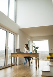 Junge Frau mit Laptop am Holztisch und Blick aus dem Fenster - UUF003206