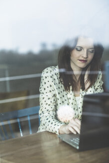 Young woman behind windowpane using laptop - UUF003214