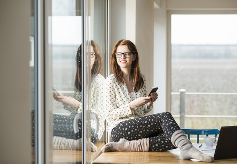 Junge Frau mit Mobiltelefon auf Holztisch sitzend, lizenzfreies Stockfoto