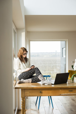 Junge Frau mit Mobiltelefon auf Holztisch sitzend, lizenzfreies Stockfoto