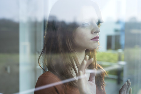 Ernste junge Frau hinter Fensterscheibe, lizenzfreies Stockfoto