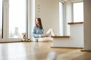 Young woman sitting on floor next to teddy bear - UUF003231