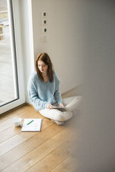 Young woman sitting on floor taking notes - UUF003232