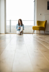 Young woman sitting on floor using cell phone - UUF003236