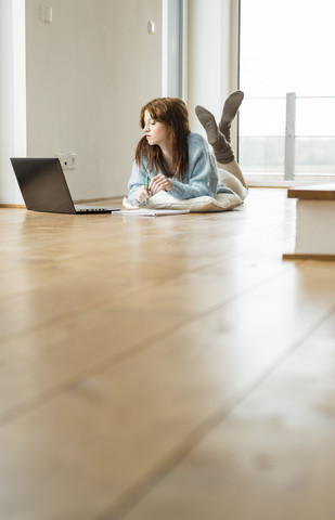 Junge Frau auf dem Boden liegend mit Laptop, lizenzfreies Stockfoto