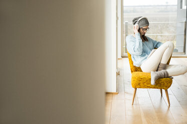 Young woman sitting on chair with digital tablet and headphones - UUF003251