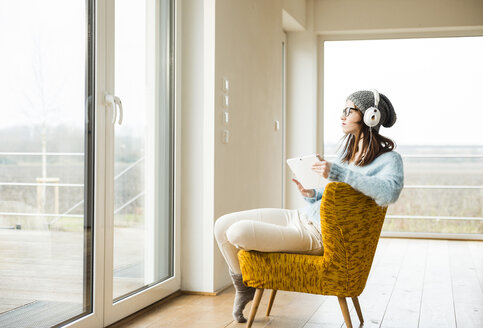 Junge Frau sitzt auf einem Stuhl mit digitalem Tablet und Kopfhörern - UUF003242