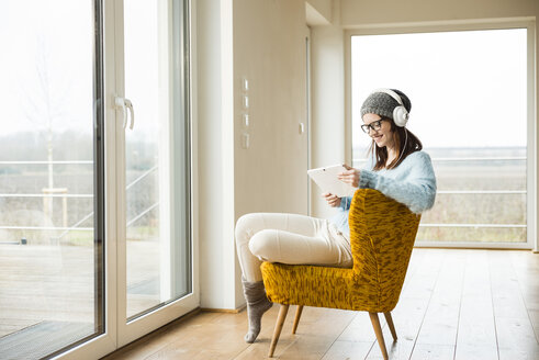 Lächelnde junge Frau auf einem Stuhl sitzend mit digitalem Tablet und Kopfhörern - UUF003243