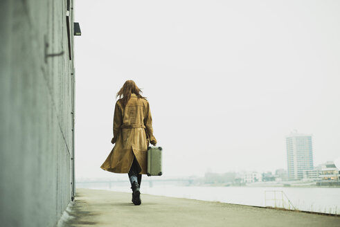 Junge Frau mit Koffer beim Spaziergang am Flussufer - UUF003258