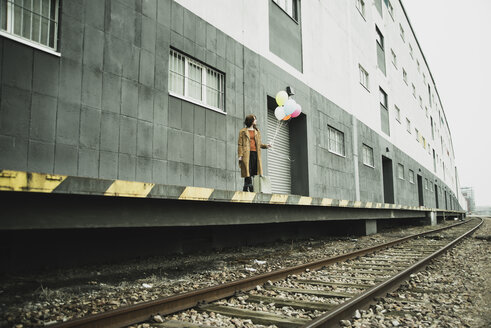 Junge Frau mit Koffer, die auf dem Bahnsteig einen Strauß Luftballons hält - UUF003263