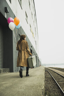 Junge Frau mit Koffer, die auf dem Bahnsteig einen Strauß Luftballons hält - UUF003264