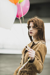 Junge Frau im Mantel hält ein Bündel Luftballons - UUF003266