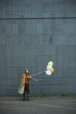 Junge Frau mit Koffer, die einen Strauß Luftballons hält, lizenzfreies Stockfoto