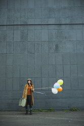 Young woman with suitcase holding bunch of balloons - UUF003278