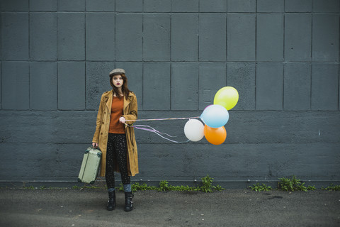 Junge Frau mit Koffer, die einen Strauß Luftballons hält, lizenzfreies Stockfoto