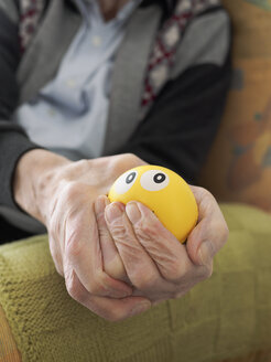 Old man in armchair squeezing stress ball - LAF001297