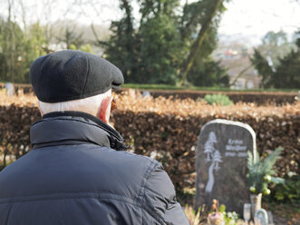 Alter Mann auf dem Friedhof betrachtet einen Grabstein - LAF001305