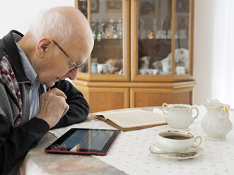 Alter Mann sitzt am Tisch und benutzt ein digitales Tablet - LAF001309