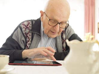 Alter Mann sitzt am Tisch und benutzt ein digitales Tablet - LAF001311