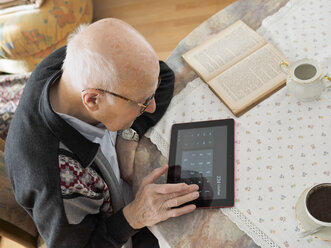 Alter Mann sitzt am Tisch und benutzt ein digitales Tablet - LAF001312