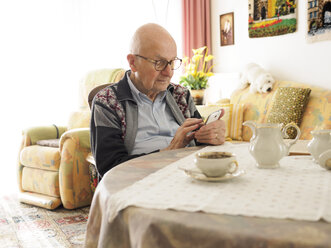 Alter Mann sitzt am Tisch und benutzt ein Mobiltelefon - LAF001313